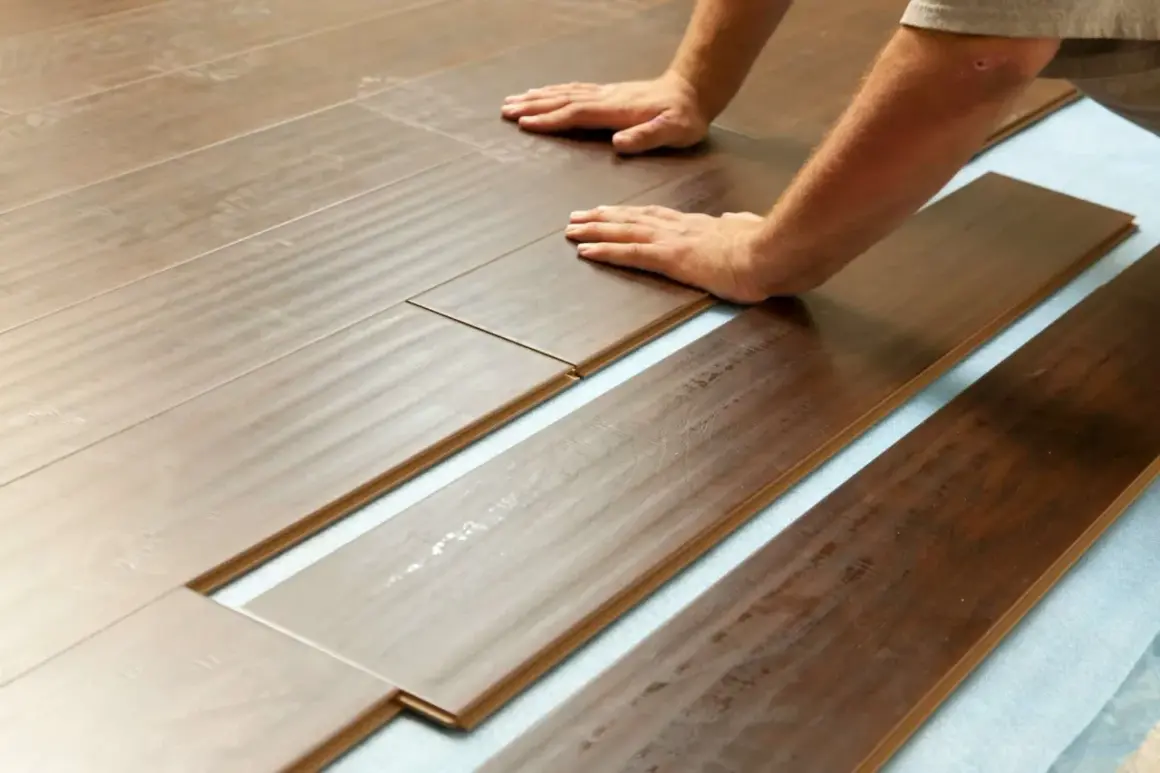 Pose de lames de parquet imitation bois sur une sous-couche bleue. L'isolation plancher bois est en cours, les mains guident l'assemblage.