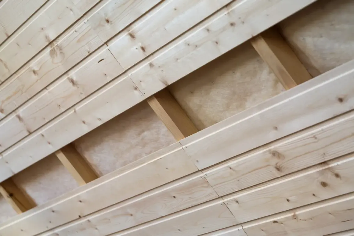 Pose lambris en bois clair, montrant la structure sous-jacente avec des tasseaux et de l'isolant.