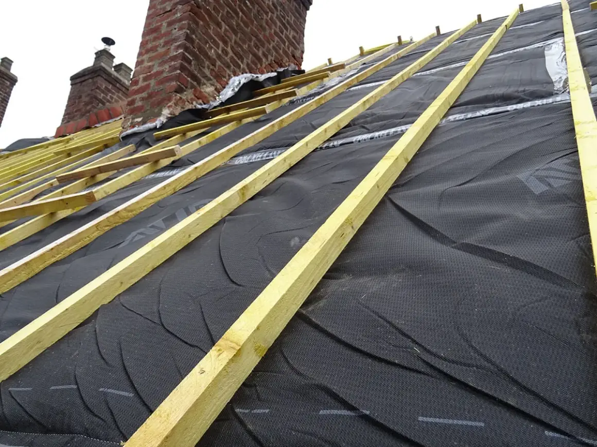Charpente en cours d'installation, avec la membrane d'étanchéité noire prête pour l'isolation toiture. Les chevrons en bois sont posés.