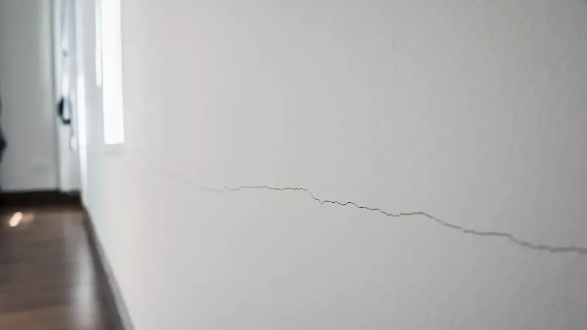 Un fin mur qui s'effrite, marqué par une longue fissure sinueuse, témoigne du passage du temps dans un couloir lumineux.