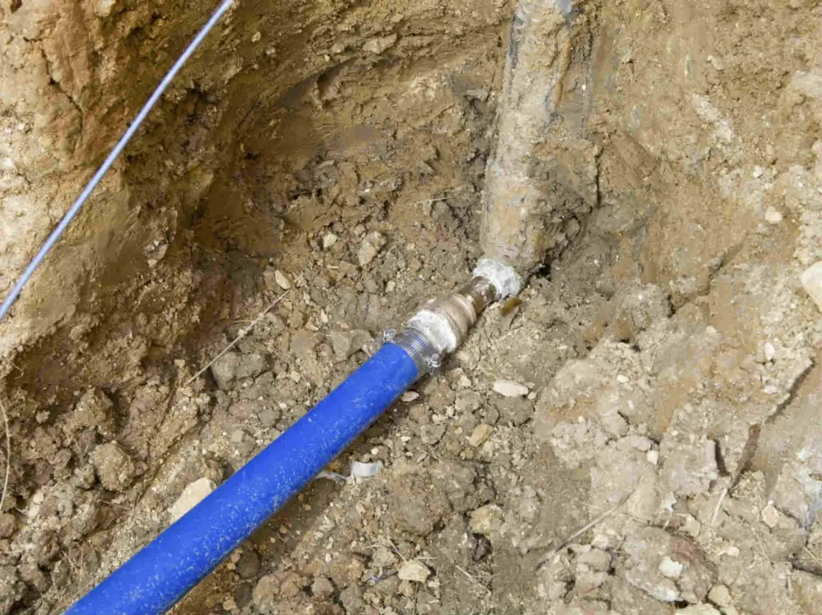 Raccordement d'une canalisation eau enterrée, respectant les normes. Le tuyau bleu est relié à une conduite plus ancienne.