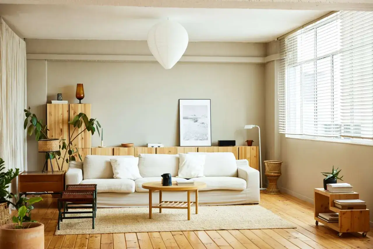 Salon lumineux avec canap&eacute; blanc, meubles en bois clair et une peinture mat ou satin sur les murs.