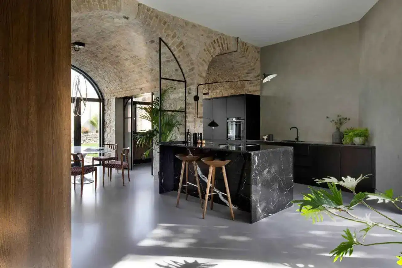 Cuisine moderne avec îlot en marbre noir, murs en briques apparentes et béton ciré sol lisse et lumineux.