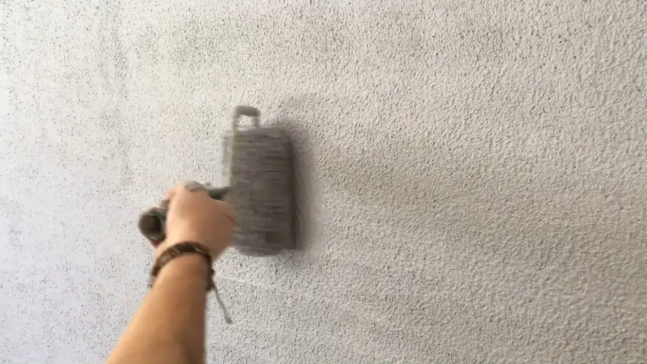 Application d'un cr&eacute;pi au rouleau sur un mur textur&eacute;. La main tient fermement l'outil pour un r&eacute;sultat uniforme.