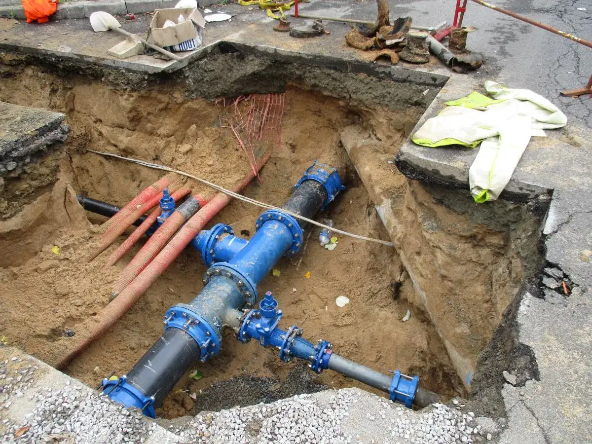 Travaux de canalisation d'eau enterrée, respectant les normes. Des tuyaux bleus et rouges sont visibles dans une tranchée.