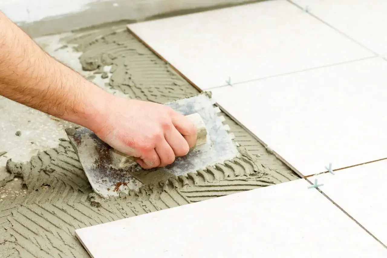 Main tenant pose la colle pour carrelage avec une truelle crantée. La pose de carrelage est en cours.