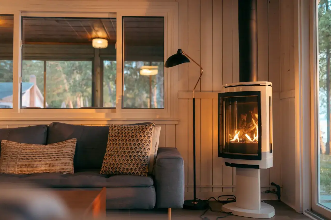 Un po&ecirc;le &agrave; bois moderne, avec un feu vif, est plac&eacute; &agrave; distance du mur en placo, cr&eacute;ant une ambiance chaleureuse.