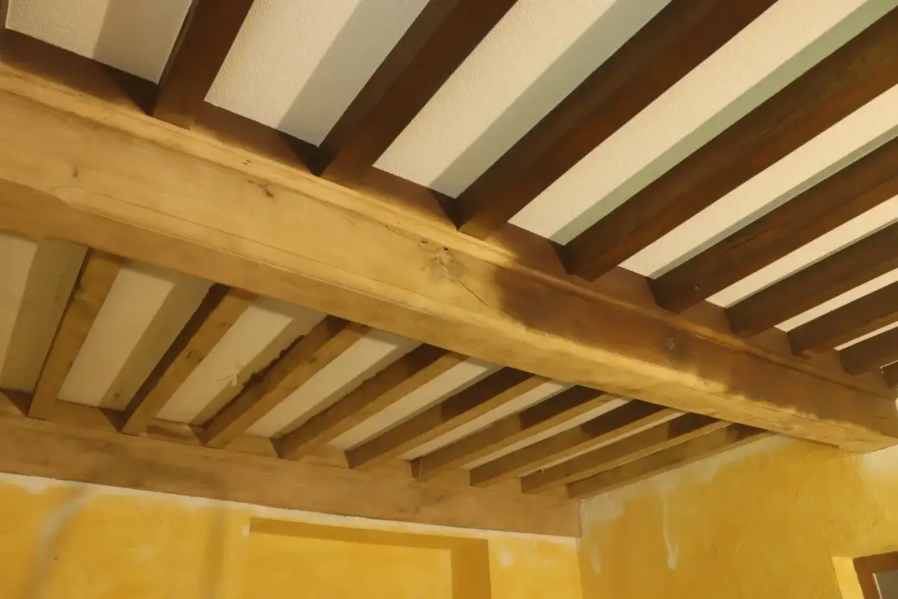 Poutres en bois massif, fraîchement sablées, révélant leur grain naturel sous un plafond blanc. Le sablage poutre bois met en valeur la beauté rustique de la charpente.