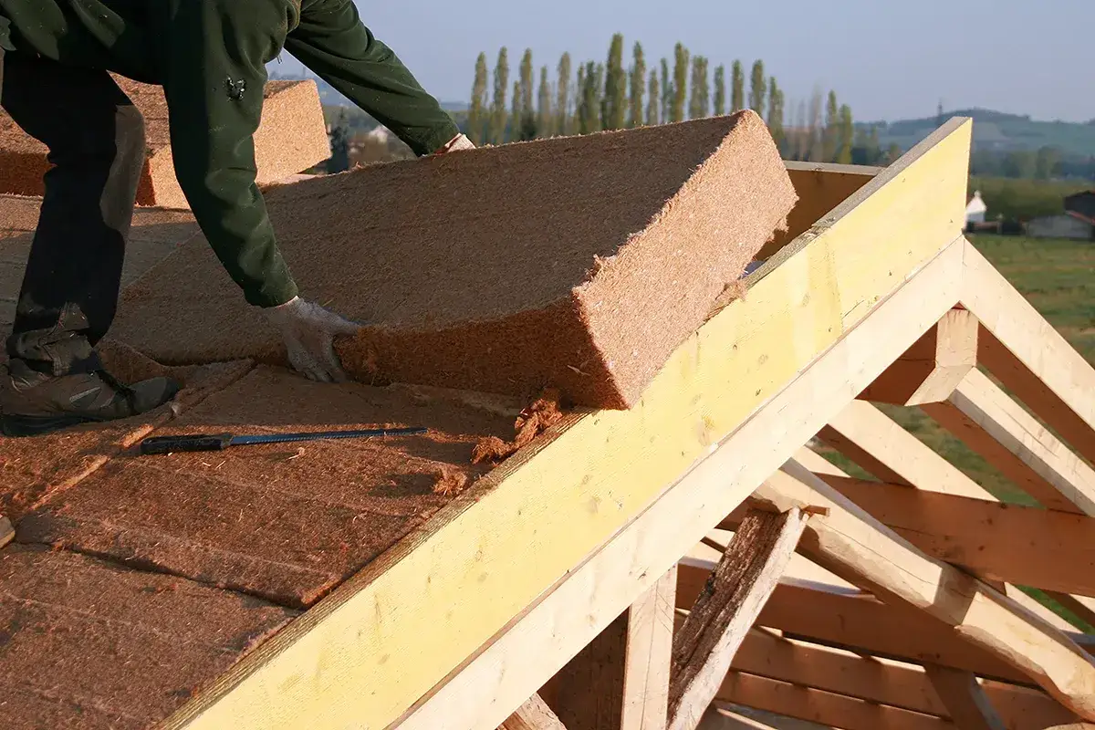 Pose d'isolant en fibre de bois sur une charpente. Un ouvrier manipule un panneau d'isolation naturel.