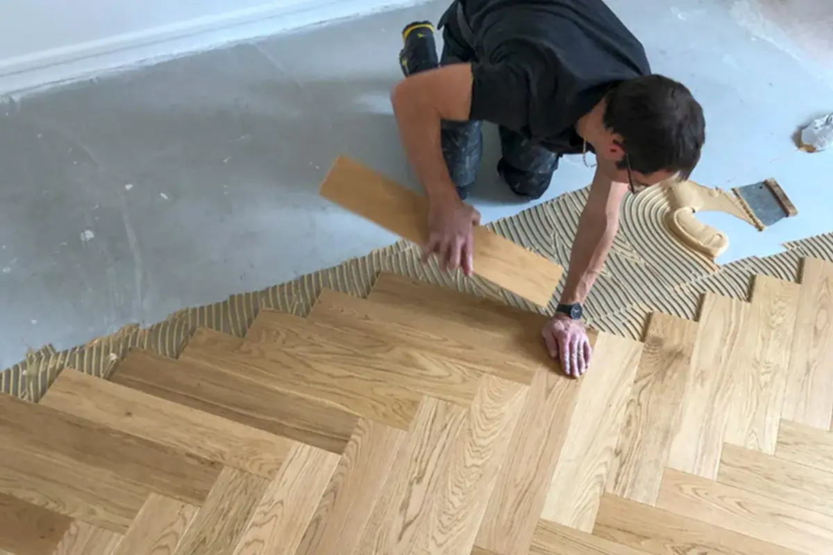 Pose baton rompu : un artisan pose un parquet en bois, cr&eacute;ant un motif en chevrons sur un sol pr&eacute;par&eacute; avec de la colle.
