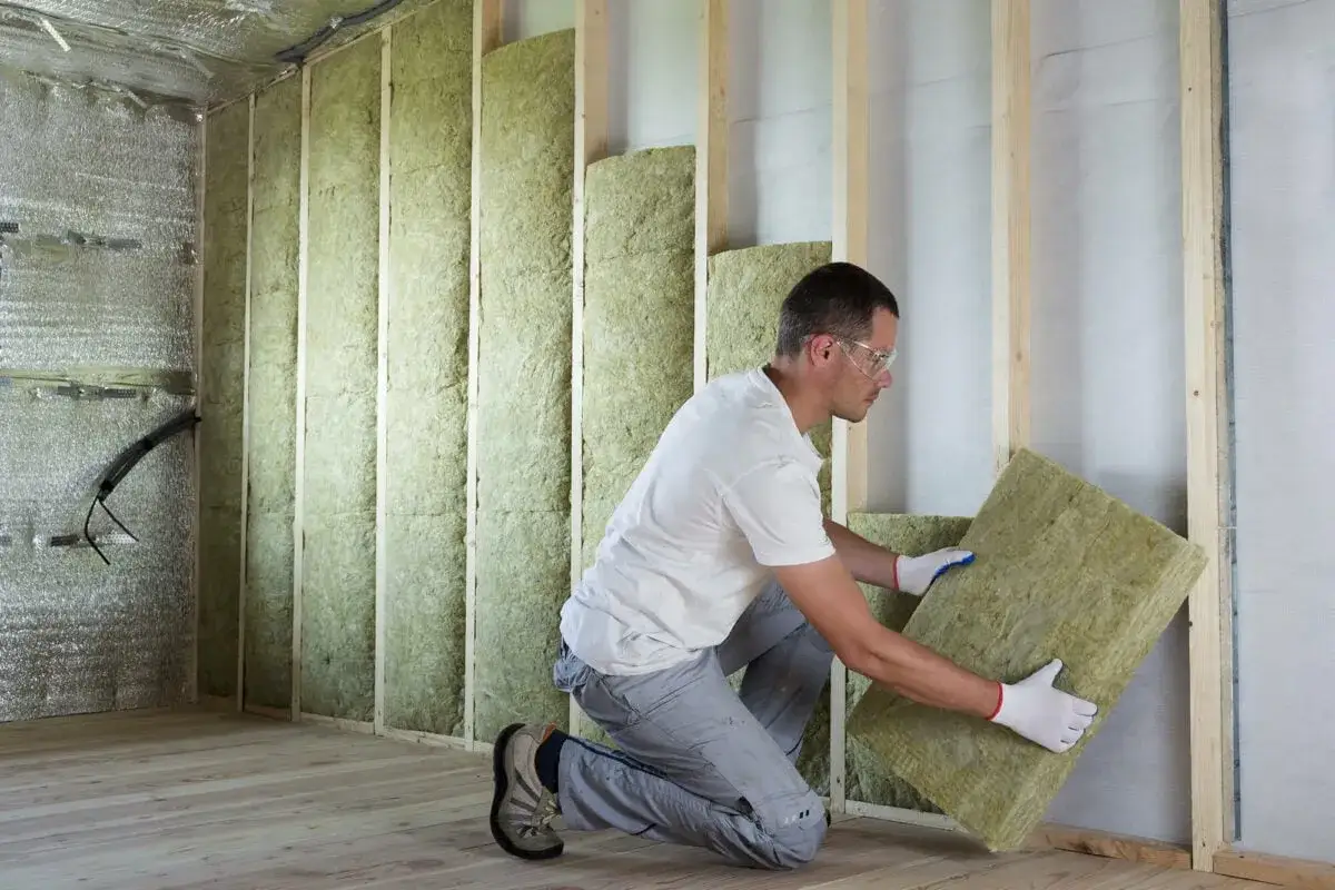 Un ouvrier installe des panneaux d'isolant minéral pour le cout isolation interieur. Les murs sont en cours de finition.
