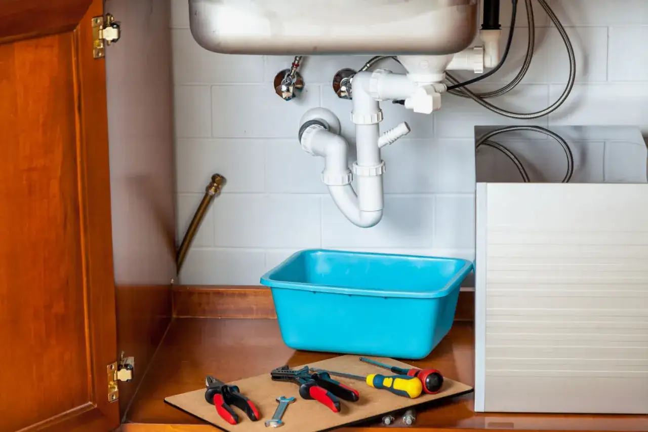 Outils et bac bleu prêts pour déboucher évier. Plomberie sous l'évier visible.