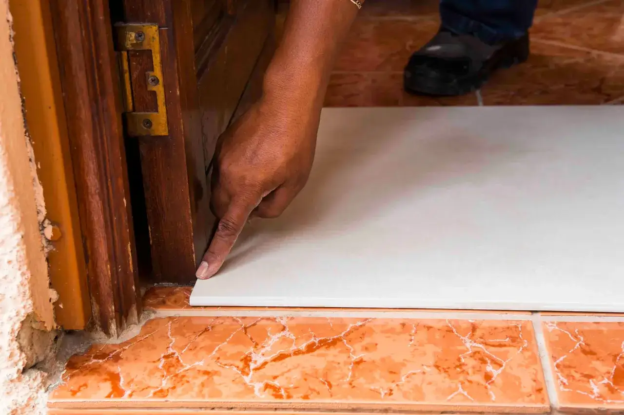 Une main v&eacute;rifie la pose d'une nouvelle dalle blanche sur une ancienne, utilisant de la colle carrelage sur carrelage pour une finition parfaite.