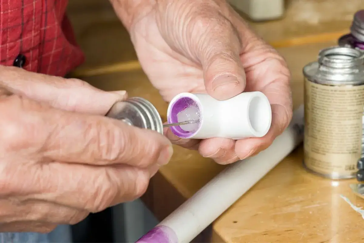 Application de colle PVC sur un raccord. Le temps de séchage colle PVC est crucial pour une installation réussie.