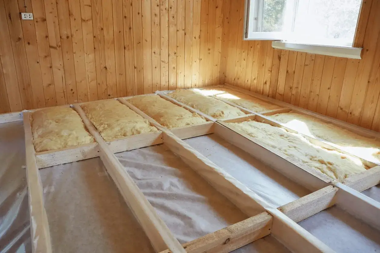 Travaux d'isolation plancher bas : pose de laine de verre dans une structure en bois.