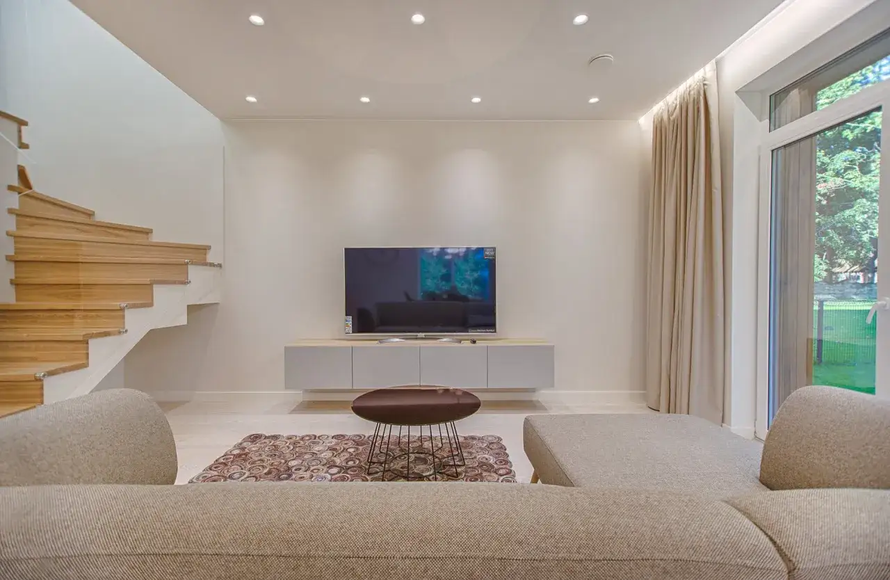 Salon moderne avec escalier en bois, canap&eacute;, t&eacute;l&eacute;vision et un &eacute;l&eacute;gant plafond tendu illumin&eacute; par des spots discrets.