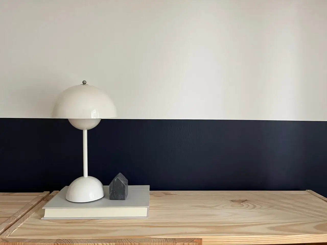 Sur un mur avec une peinture salon deux tons, une lampe blanche repose sur des livres, &agrave; c&ocirc;t&eacute; d'une petite maison en pierre.