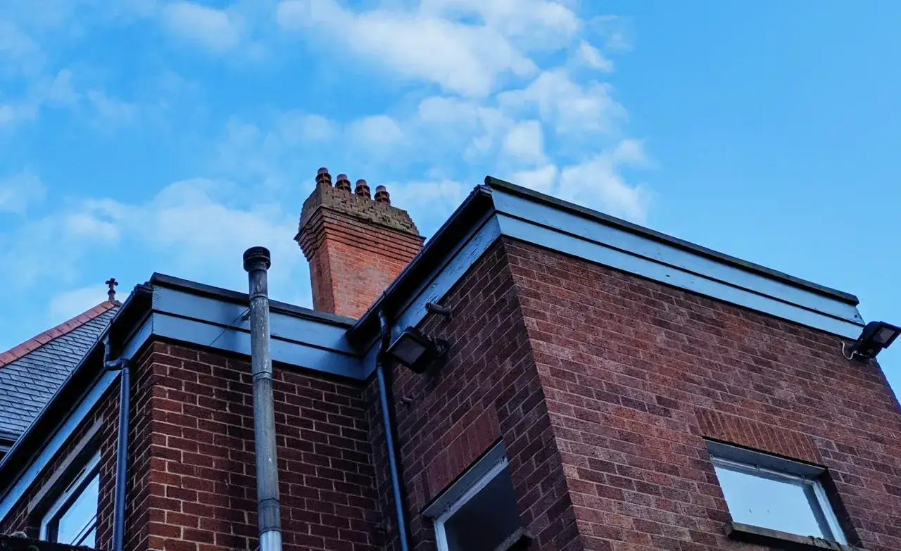 Vue d'une maison en briques rouges sous un ciel bleu nuageux. Un conduit de po&ecirc;le &agrave; bois est visible sur le c&ocirc;t&eacute;.