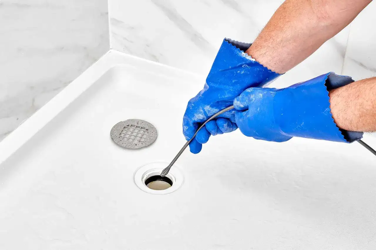 Mains bleues, outil de plomberie dans une douche blanche pour déboucher la douche.