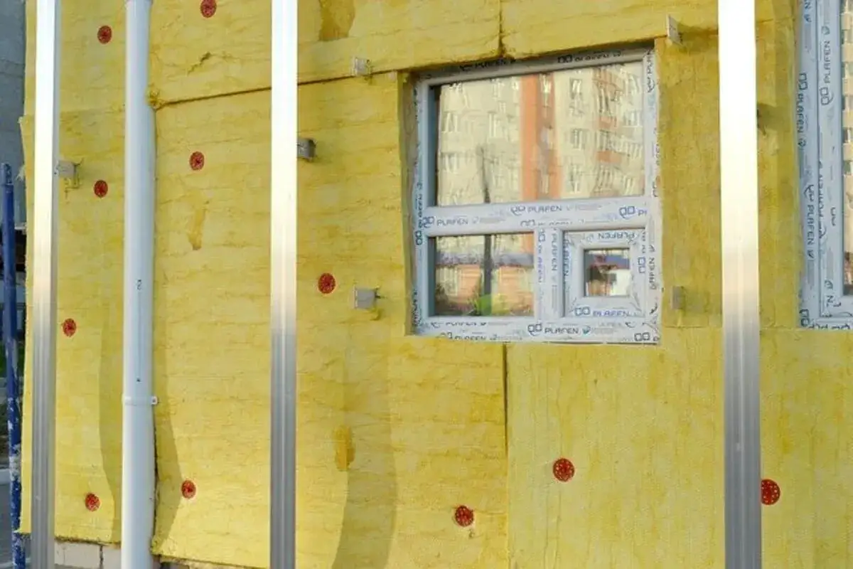 Isolation thermique d'un mur avec un mat&eacute;riau jaune, des fixations rouges et des profil&eacute;s m&eacute;talliques. Une fen&ecirc;tre est visible.
