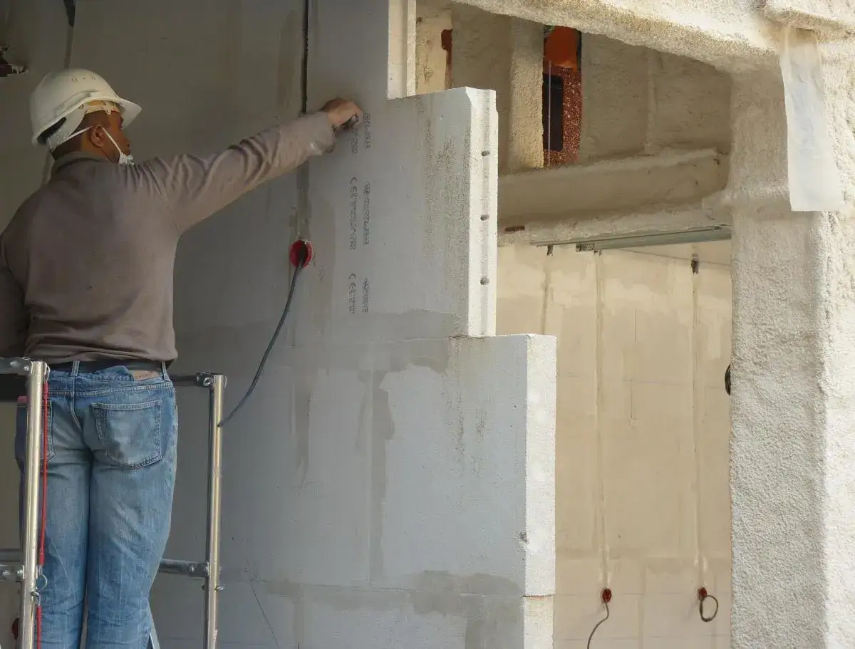 Un ouvrier sur un &eacute;chafaudage pose des blocs de b&eacute;ton cellulaire pour l'isolation d'un mur.