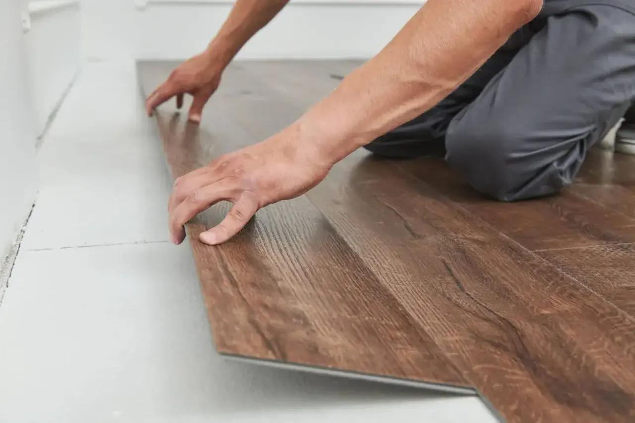 Pose d'un parquet flottant imitation bois. Mains ajustant une lame de rev&ecirc;tement de sol.