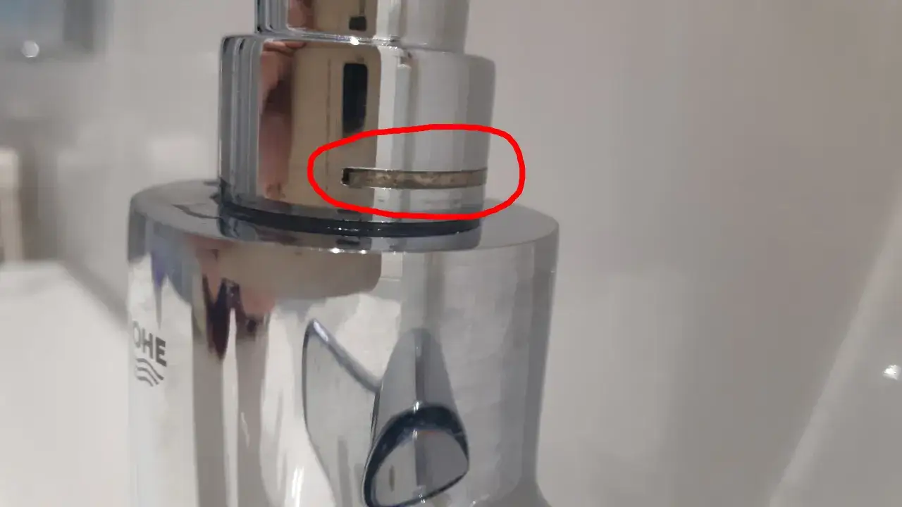Gouttes d'eau s'&eacute;chappent d'un robinet mitigeur qui fuit au col, pr&egrave;s d'une zone calcaire.