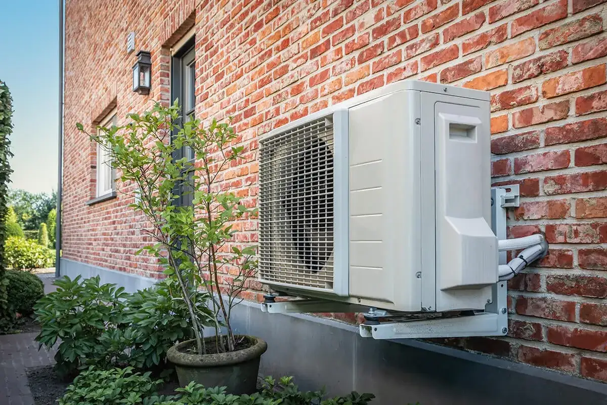 Unit&eacute; ext&eacute;rieure d'une pompe &agrave; chaleur air air, fix&eacute;e sur un mur de briques rouges. Avis sur son efficacit&eacute; &eacute;nerg&eacute;tique.