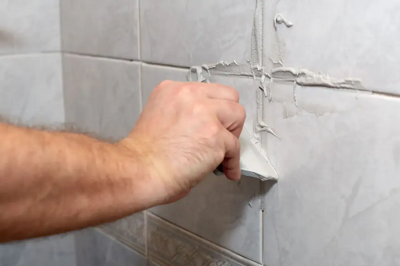 Main d'un artisan en train d'enlever joint carrelage avec une spatule sur un mur carrel&eacute;.