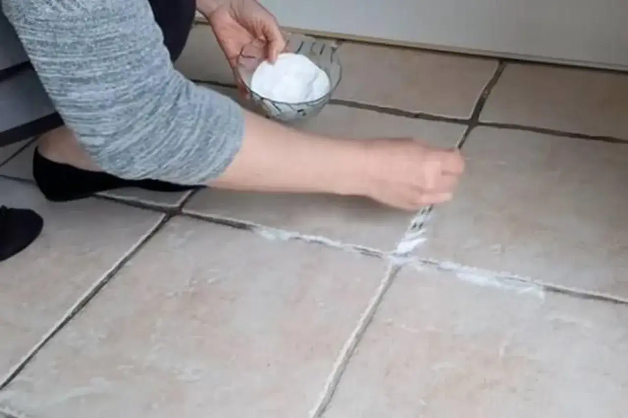 Une personne nettoie les joints de carrelage avec une pâte blanche, espérant faire disparaître une tache sur carrelage qui ne part pas.