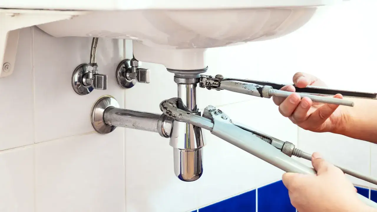 Mains tenant des clés pour démonter le siphon de la baignoire.