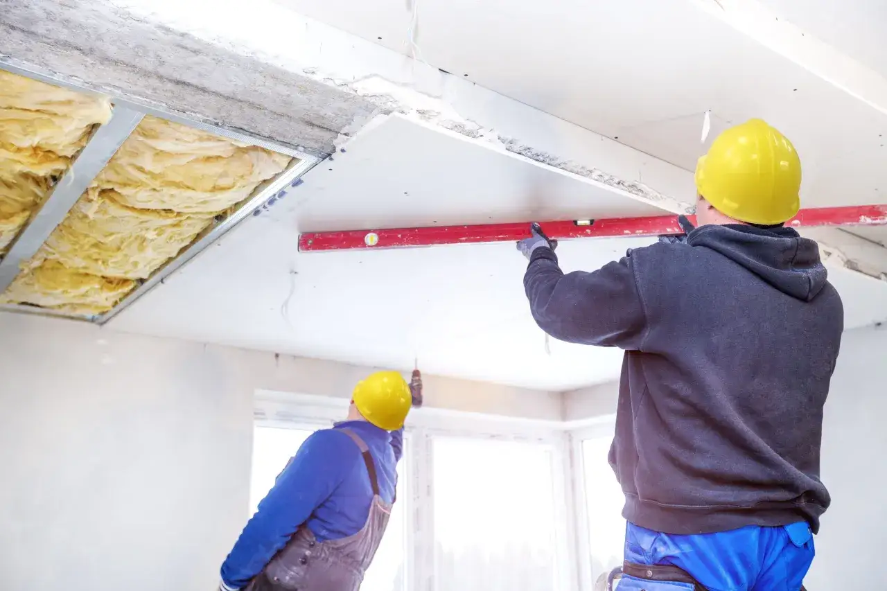 Pose de l'isolation du plafond d'un appartement. Des ouvriers en casque jaune installent des panneaux de pl&acirc;tre et v&eacute;rifient le niveau.
