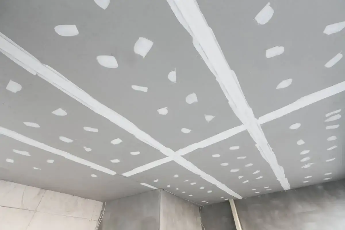 Plafond en cours de finition, avec des bandes de jointoiement blanches sur les plaques de plâtre. Travail de coller placo plafond.