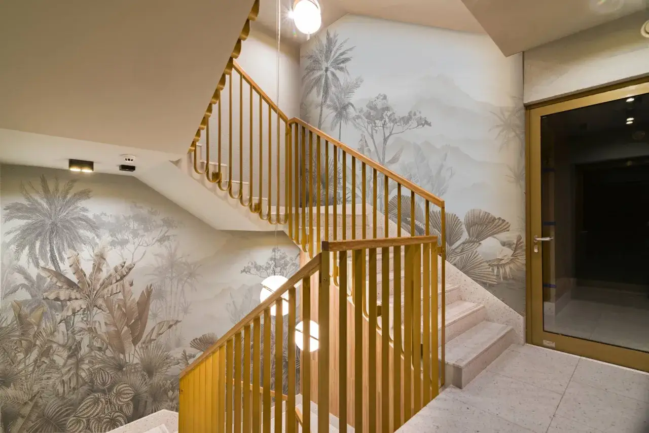 Habillage mur cage d'escalier avec un d&eacute;cor tropical en cama&iuml;eu. Escalier en marbre et rambarde en bois dor&eacute;.