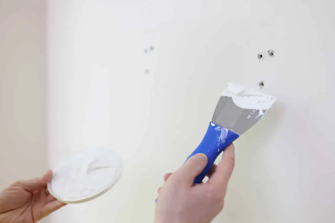 Application de mastic &agrave; l'aide d'une spatule pour reboucher des trous dans un mur blanc.