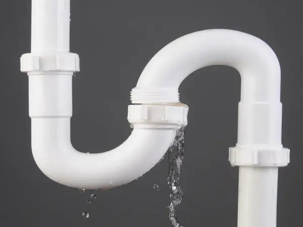 Tuyau de PVC blanc avec une fuite d'eau. Le temps de séchage de la colle PVC est crucial pour éviter ce genre de problème.
