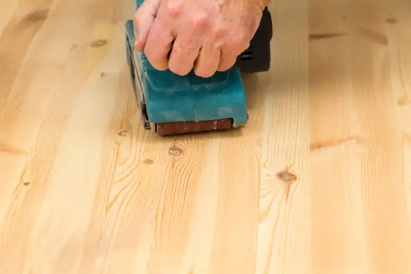 Main d'une personne utilisant une ponceuse pour poncer un parquet en bois clair.