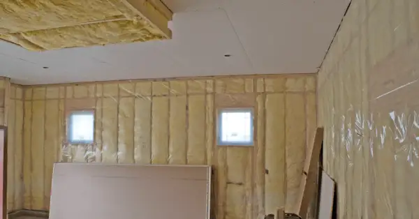 Isolation plafond garage en cours, murs recouverts de laine de verre et pare-vapeur. Deux petites fenêtres laissent passer la lumière.