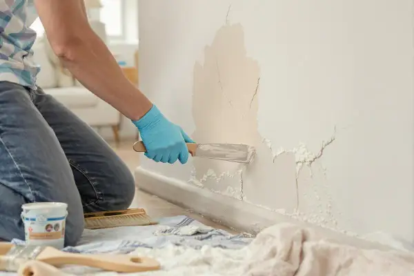 Un artisan répare une fissure sur un mur intérieur avec une spatule.