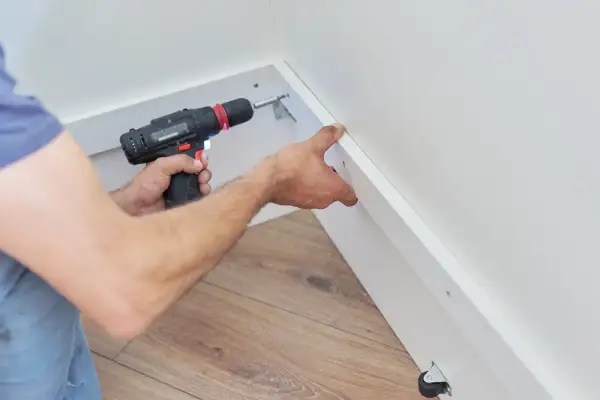 Un bricoleur utilise une visseuse pour fixer du placo sous pente, créant ainsi un espace de rangement fonctionnel.