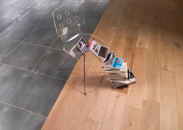 Une jonction carrelage parquet sans barre de seuil, avec une chaise transparente et des livres.