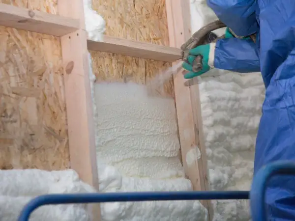 Application de polyuréthane projeté pour isoler une structure en bois. La mousse blanche s'étend, créant une barrière isolante.