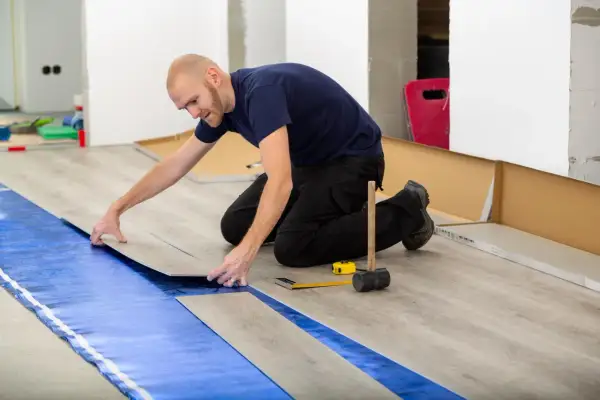 Pose d'un revêtement de sol stratifié sur une isolation sous carrelage. L'homme pose une lame de parquet.