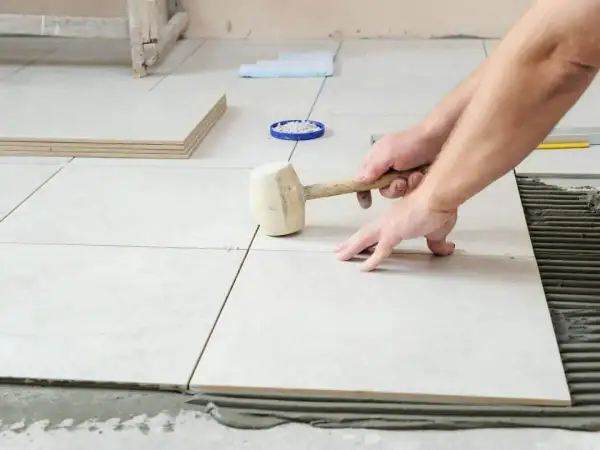 Pose de carrelage : un artisan utilise un maillet pour ajuster une nouvelle dalle sur le mortier.