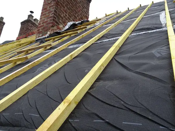 Charpente en cours d'installation, avec la membrane d'étanchéité noire prête pour l'isolation toiture. Les chevrons en bois sont posés.