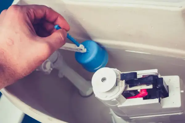 Main tenant ajuste le flotteur bleu pour arrêter la chasse d'eau qui coule.