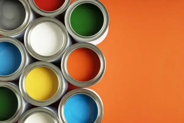 Un assortiment de pots de peinture glycero ou acrylique ouverts, révélant des couleurs vives comme le bleu, le jaune, le rouge, le vert et l'orange sur fond orange.