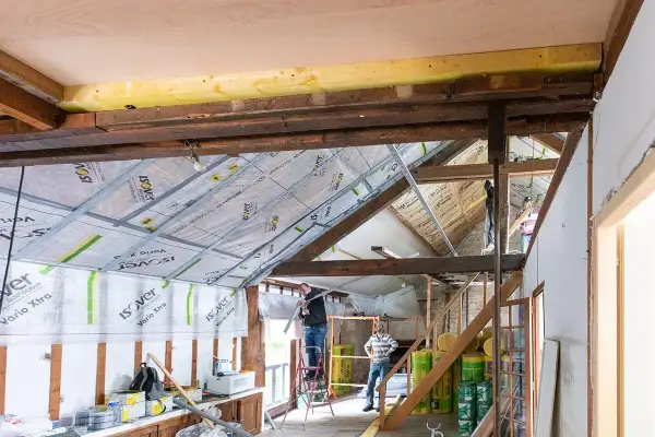 Travaux en cours pour refaire un plafond. Des ouvriers installent des rails métalliques sous les poutres apparentes.