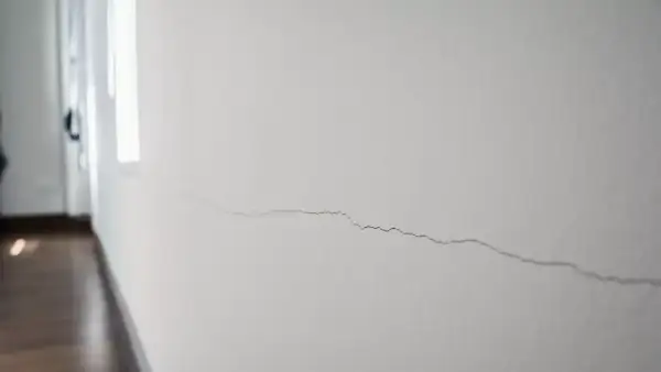 Un fin mur qui s'effrite, marqué par une longue fissure sinueuse, témoigne du passage du temps dans un couloir lumineux.