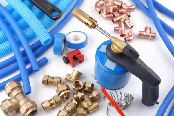 Outils pour une installation multicouche : chalumeau, tubes bleus, raccords en laiton et cuivre, coupe-tube.